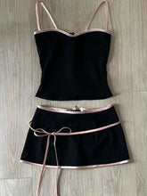 Black two-piece outfit with thin straps and a belt on a wooden surface